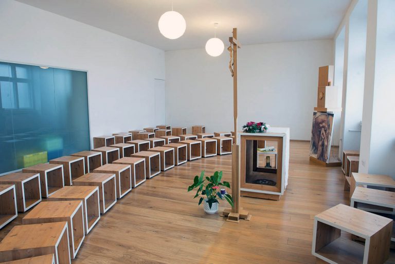 Celkový pohľad na priestor kaplnky. Priestorové obmedzenie pôvodnej školskej učebne bolo pretvorené v otvorený, čistý priestor s jasne čitateľným zariadením.